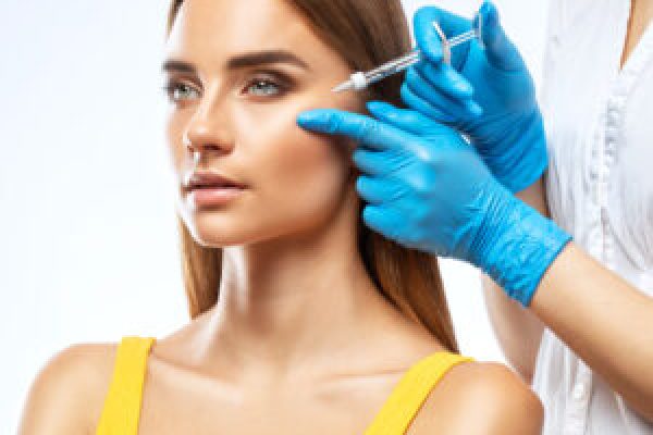 Cosmetologist makes rejuvenating anti wrinkle injections on the face of a beautiful woman in a yellow blouse. Female aesthetic cosmetology in a beauty salon.